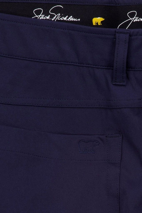 Nahaufnahme einer dunkelblauen Jack Nicklaus Hose mit sichtbarem Bund, Etikett mit Signatur und gelbem Bärlogo sowie eingewebtem Bärlogo auf der Tasche