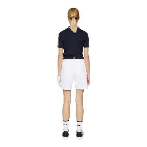 Rückansicht einer Frau in einem schwarzen Poloshirt und weißer Shorts, die auf einem neutralen Hintergrund steht