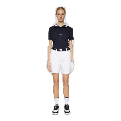 Weibliches Golfmodell trägt marineblaues Poloshirt, weiße Shorts und schwarze Sneaker