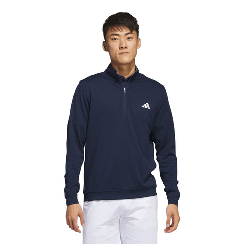Mann trägt einen dunkelblauen Adidas Pullover mit halbem Reißverschluss und weißer Hose