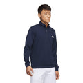 Mann trägt einen marineblauen Adidas Pullover mit Reißverschluss und weiße Hose